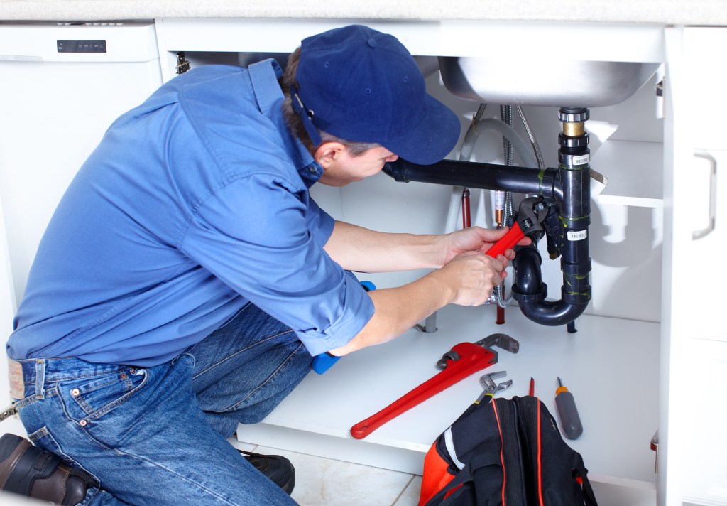 Mature plumber fixing a sink in a kitchen